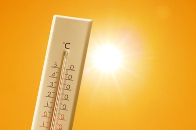 Image of Thermometer showing high temperature against orange sky with bright sun. Extremely hot weather