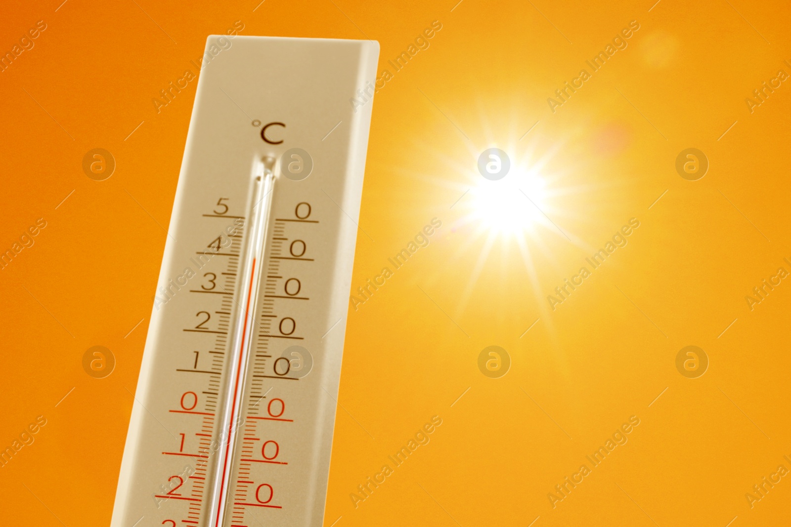 Image of Thermometer showing high temperature against orange sky with bright sun. Extremely hot weather
