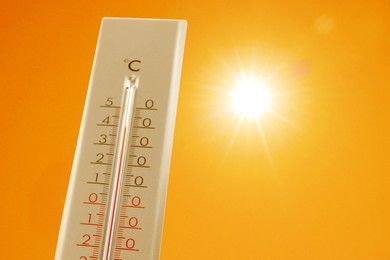 Image of Thermometer showing high temperature against orange sky with bright sun. Extremely hot weather