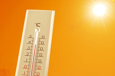Image of Thermometer showing high temperature against orange sky with bright sun. Extremely hot weather
