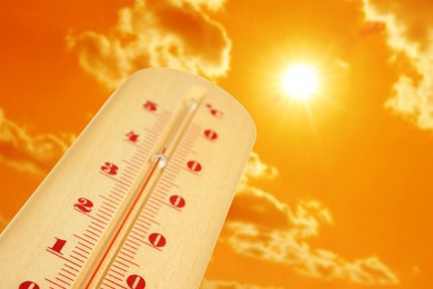 Image of Thermometer showing high temperature against orange sky with bright sun and clouds. Extremely hot weather