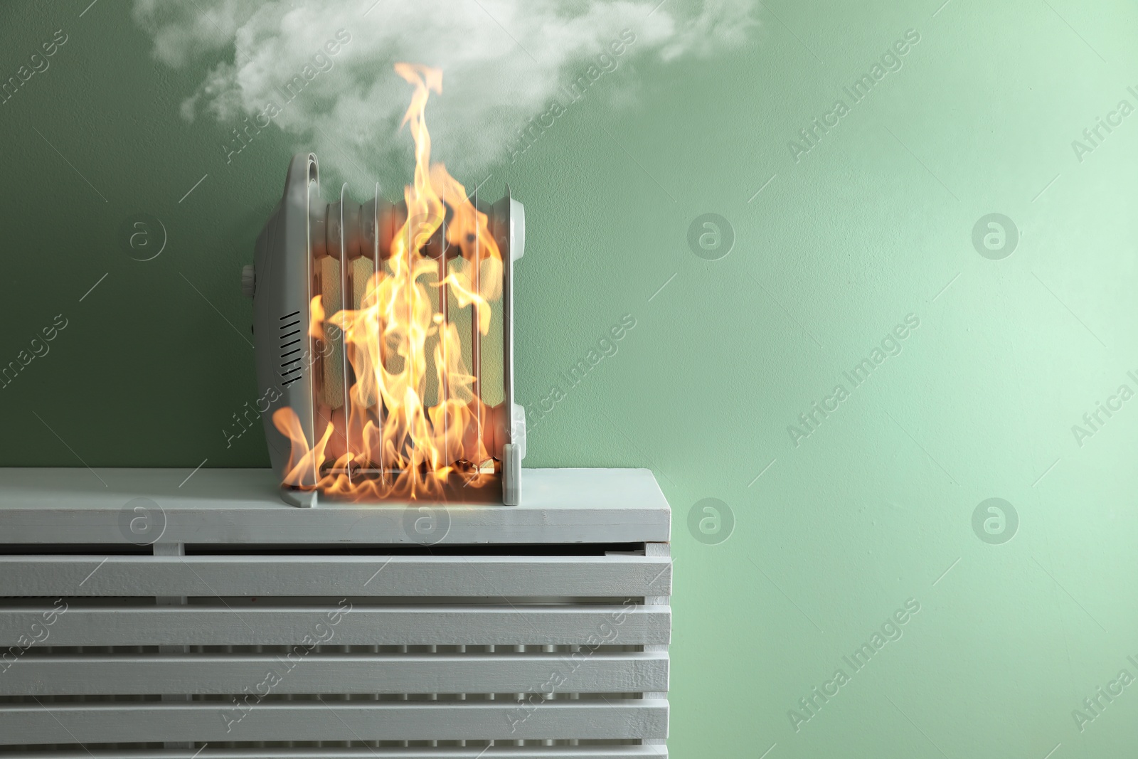 Image of Burning heater near green wall in room. Flames all over device