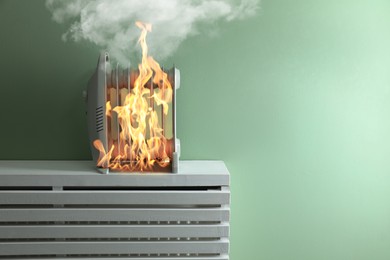 Image of Burning heater near green wall in room. Flames all over device