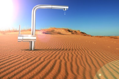Image of Save water concept. Tap with dripping water in desert under scorching sun