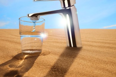 Image of Save water concept. Glass under tap with dripping water in desert
