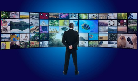 Image of Media library. Man standing in front of collection of video files on virtual screen against blue background