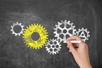 Image of Woman drawing cogwheels on black chalkboard, closeup. Gear mechanism