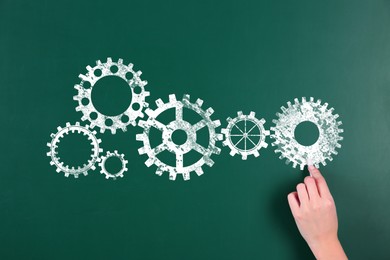 Image of Woman drawing cogwheels on green chalkboard, closeup. Gear mechanism