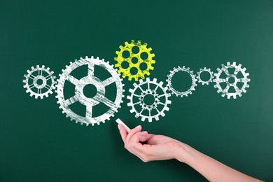 Image of Woman pointing at cogwheels drawn on green chalkboard, closeup. Gear mechanism