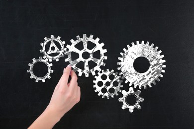 Image of Woman drawing cogwheels on black chalkboard, closeup. Gear mechanism