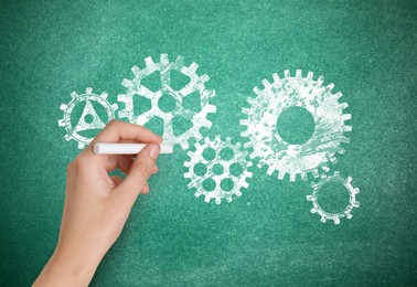 Image of Woman drawing cogwheels on green chalkboard, closeup. Gear mechanism