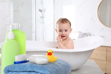 Image of Cute little baby in bathtub, accessories and toiletries indoors