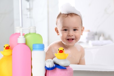 Image of Cute little baby in bathtub, accessories and toiletries indoors