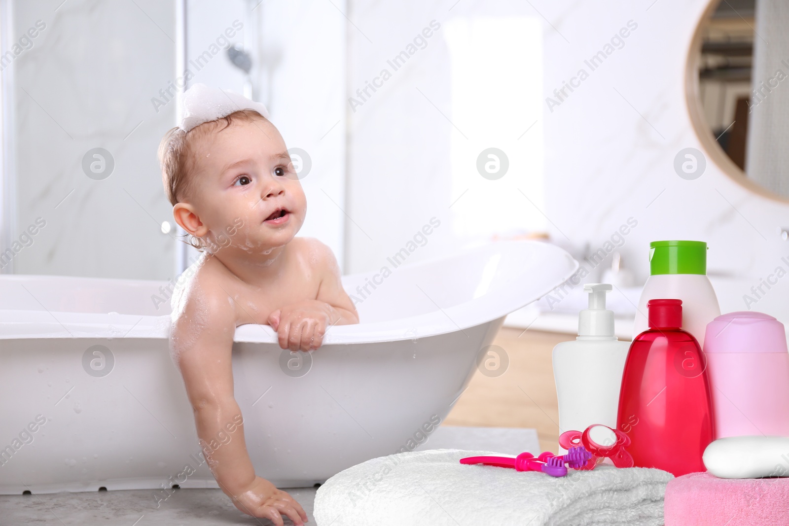Image of Cute little baby in bathtub, accessories and toiletries indoors