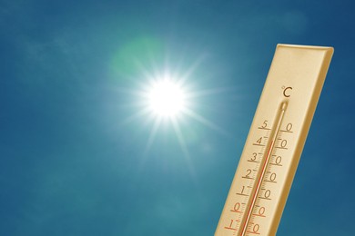 Image of Thermometer showing high temperature against sky with bright sun. Extremely hot weather
