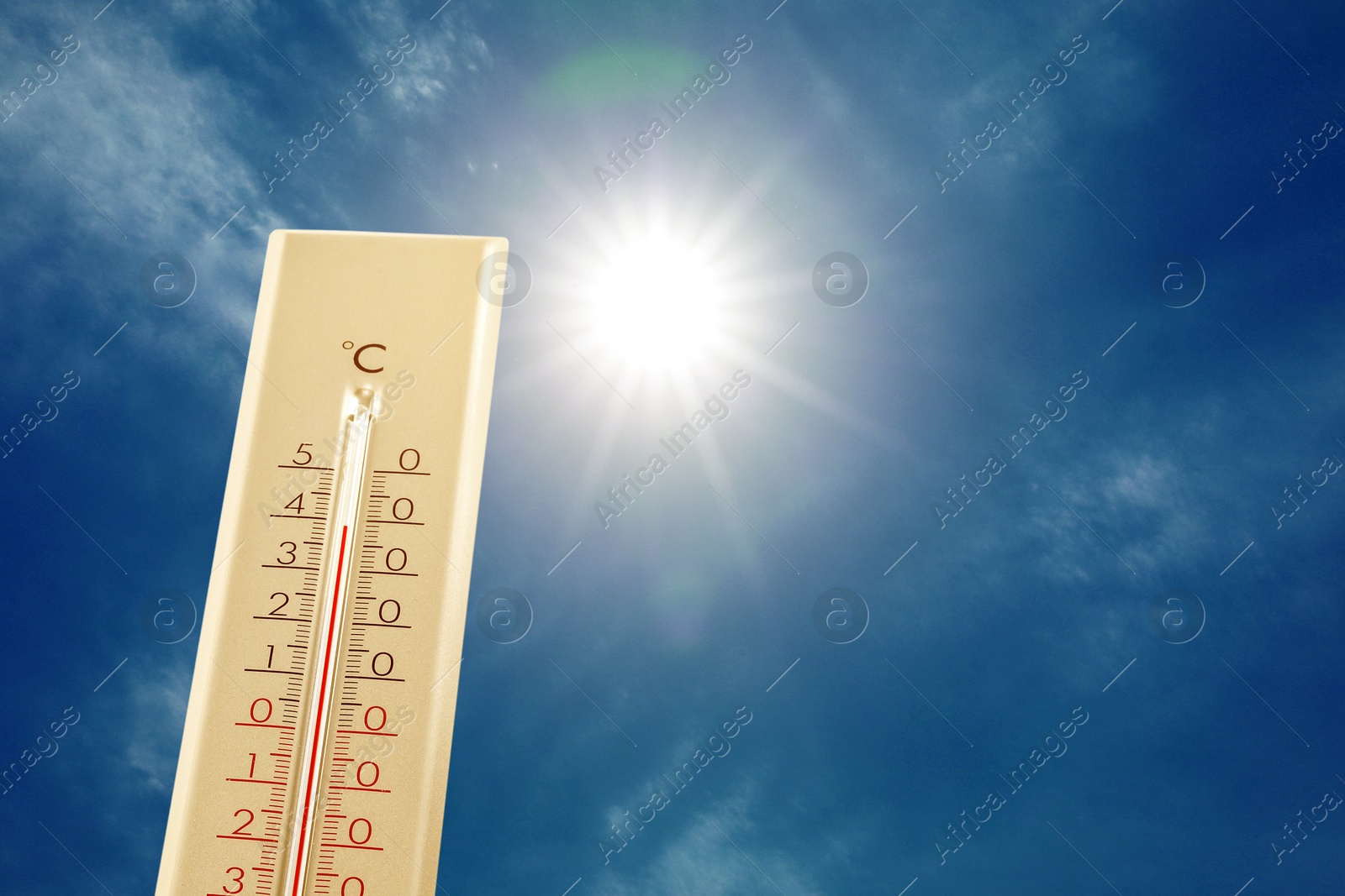 Image of High temperature on thermometer against blue sky with clouds and bright sun. Extremely hot weather