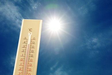Image of High temperature on thermometer against blue sky with clouds and bright sun. Extremely hot weather