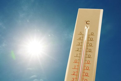 Image of Thermometer showing high temperature against sky with bright sun. Extremely hot weather