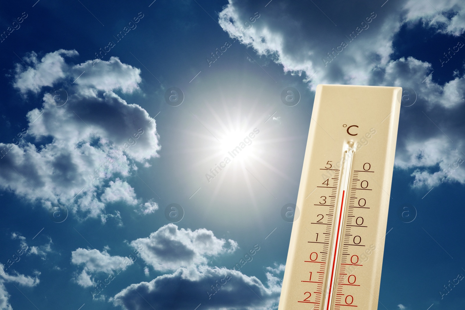 Image of High temperature on thermometer against blue sky with clouds and bright sun. Extremely hot weather