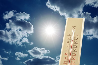 Image of High temperature on thermometer against blue sky with clouds and bright sun. Extremely hot weather