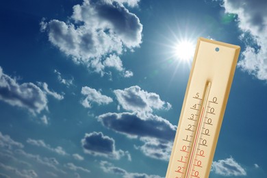Image of High temperature on thermometer against blue sky with clouds and bright sun. Extremely hot weather
