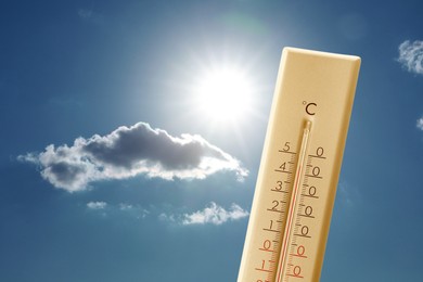 Image of High temperature on thermometer against blue sky with clouds and bright sun. Extremely hot weather