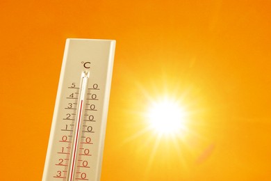 Image of Thermometer showing high temperature against orange sky with bright sun. Extremely hot weather
