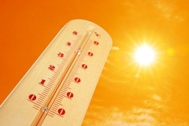 Image of Thermometer showing high temperature against orange sky with bright sun and clouds. Extremely hot weather