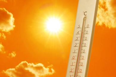 Image of Thermometer showing high temperature against orange sky with bright sun and clouds. Extremely hot weather