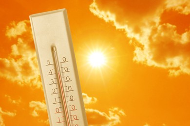 Image of Thermometer showing high temperature against orange sky with bright sun and clouds. Extremely hot weather
