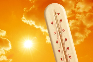 Image of Thermometer showing high temperature against orange sky with bright sun and clouds. Extremely hot weather