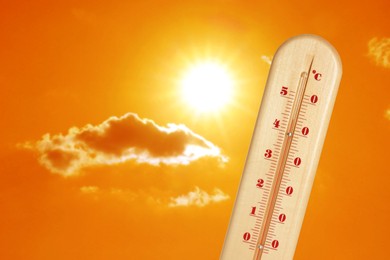 Image of Thermometer showing high temperature against orange sky with bright sun and clouds. Extremely hot weather