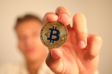 Photo of Cryptocurrency. Man holding golden bitcoin against blurred grey background, closeup