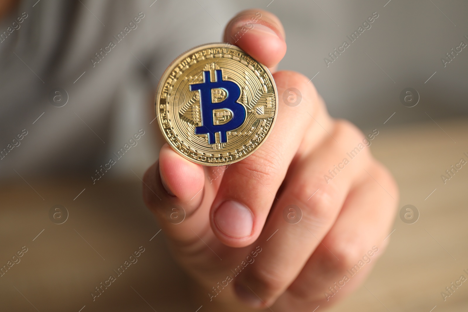 Photo of Cryptocurrency. Man holding golden bitcoin against blurred background, closeup