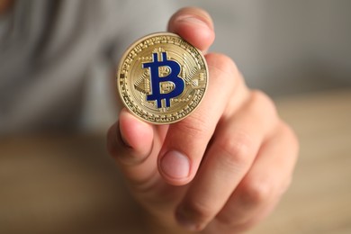 Photo of Cryptocurrency. Man holding golden bitcoin against blurred background, closeup