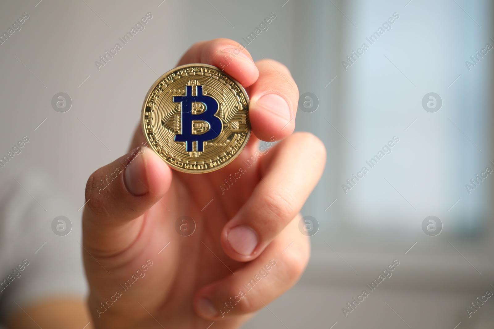 Photo of Cryptocurrency. Man holding golden bitcoin against blurred background, closeup. Space for text