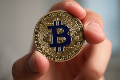 Photo of Cryptocurrency. Man holding golden bitcoin against blurred grey background, closeup