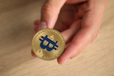 Photo of Cryptocurrency. Man with golden bitcoin at wooden table, closeup