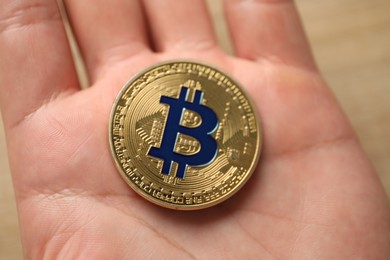 Photo of Cryptocurrency. Man with golden bitcoin at table, closeup
