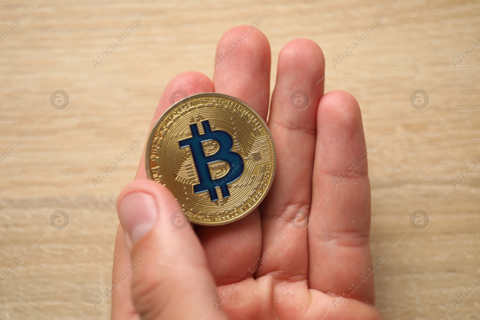 Photo of Cryptocurrency. Man with golden bitcoin at wooden table, closeup