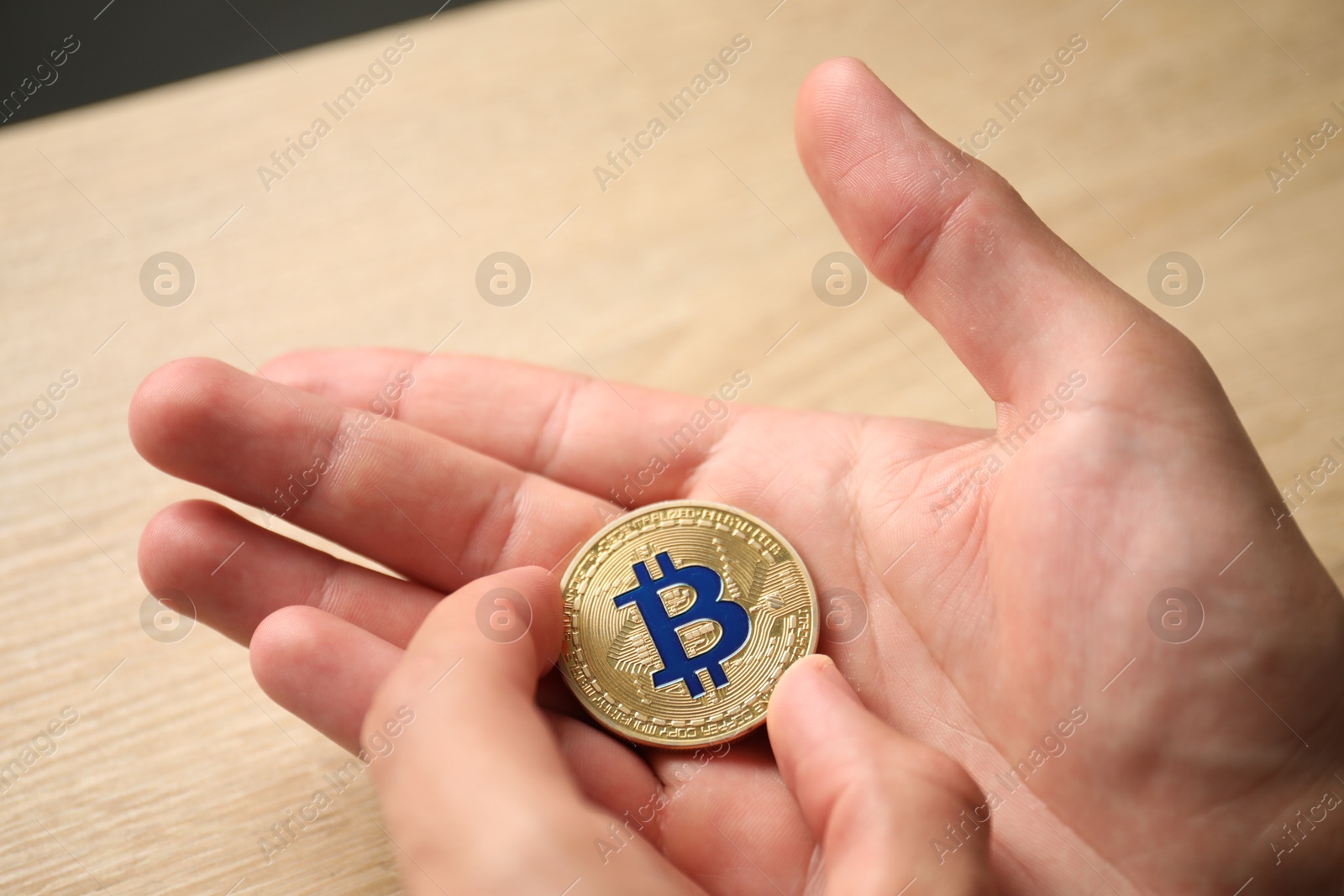 Photo of Cryptocurrency. Man with golden bitcoin at wooden table, closeup