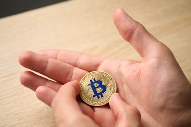 Photo of Cryptocurrency. Man with golden bitcoin at wooden table, closeup