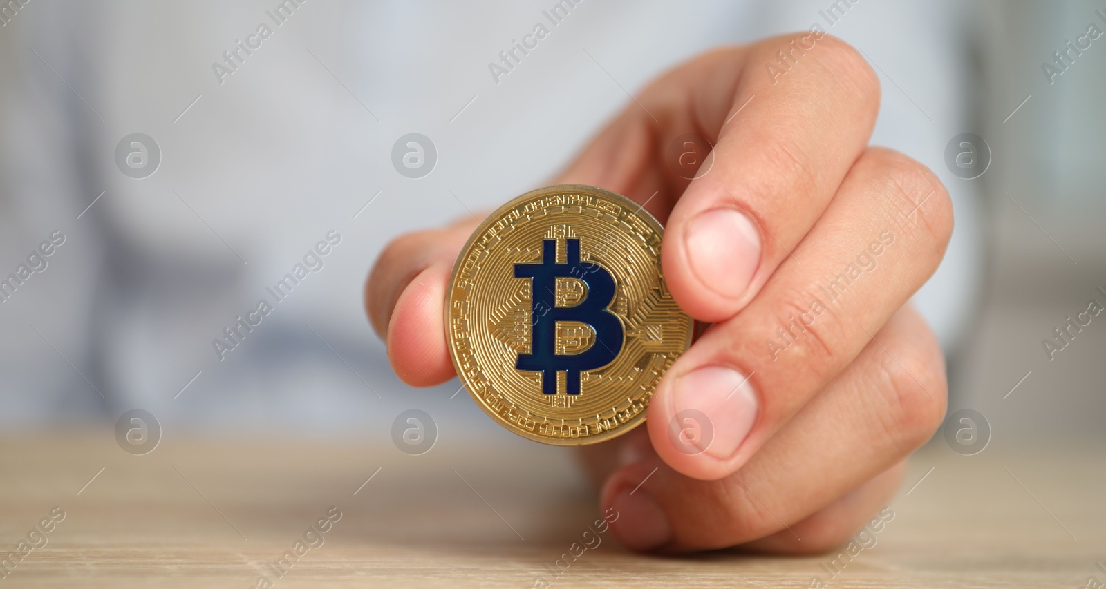 Photo of Cryptocurrency. Man with golden bitcoin at wooden table against blurred background, closeup. Space for text