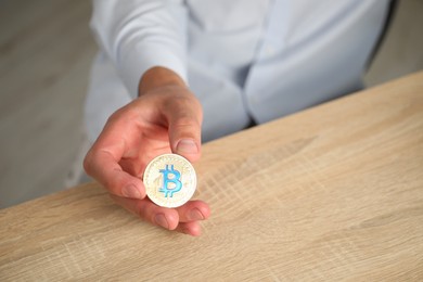 Photo of Cryptocurrency. Man with golden bitcoin at wooden table indoors, closeup