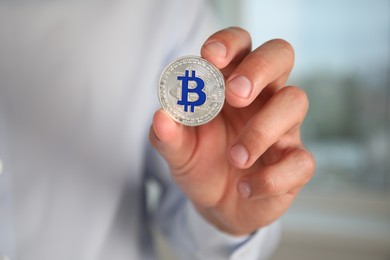 Photo of Cryptocurrency. Man with silver bitcoin on blurred background, closeup. Space for text