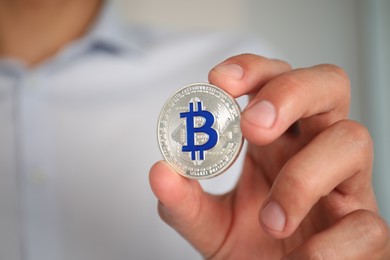 Photo of Cryptocurrency. Man with silver bitcoin on blurred background, closeup. Space for text