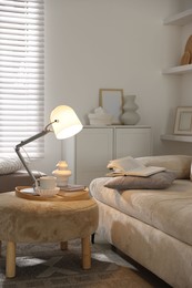 Photo of Stylish lamp, vase, books and cup on pouf near sofa indoors