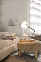 Photo of Stylish lamp, vase, books and cup on pouf near sofa indoors