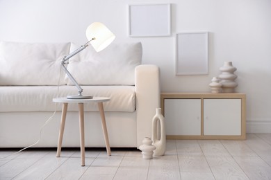 Photo of Stylish lamp on table and vases near sofa indoors