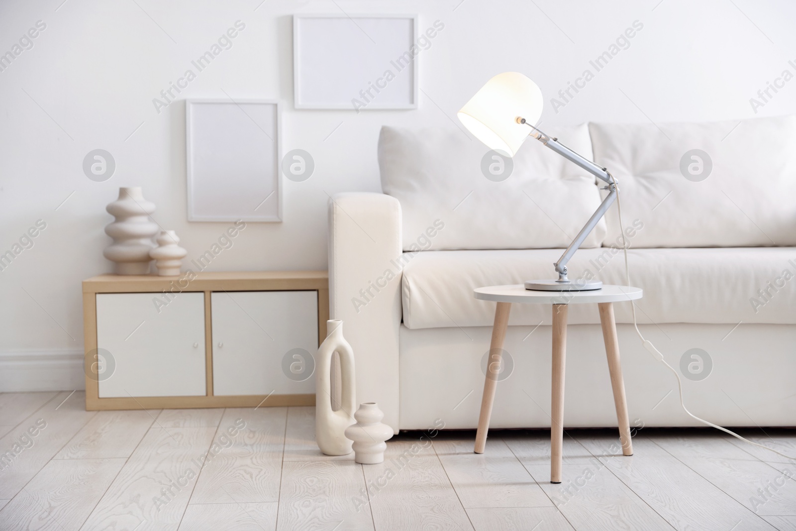 Photo of Stylish lamp on table and vases near sofa indoors